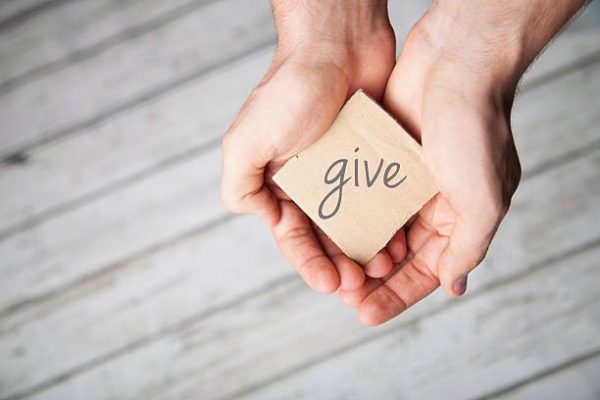 Two Hands holding a small sign that says give.