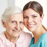 An elderly woman and young lady stand side by side, smiling. 