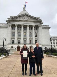 Two women and a man stand in front of the Wisconsin State Capitol building.