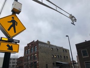 A yellow pedestrian sign with flashing lights attached to a pole.