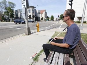 Man with cane sitting on bench next to intersection
