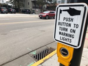 A sign reading "push button to turn on warning lights" mounted above a button on a street pole.