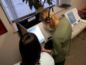 Two women stand in front of an accessible voting machine.