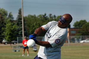 A man swings a bat at a ball while wearing a blindfold.