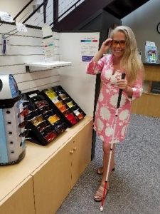 A woman tries on a pair of sunglasses while holding her white cane.