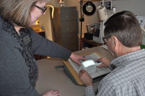 A woman points to a magnifier that a man is holding over a newspaper.