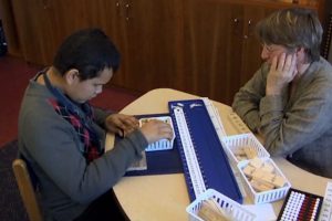 A boy and woman sit at a table with wooden blocks.
