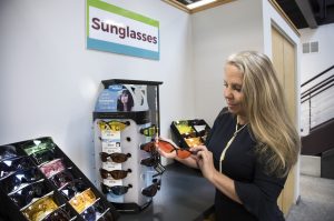 A woman stands in front of a sunglass display holding a pair of sunglasses.