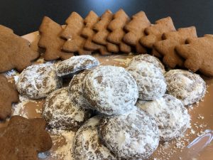 Pfeffernüsse cookies in the center of a light brown plate with gingerbread holiday trees around the edge of the plate.