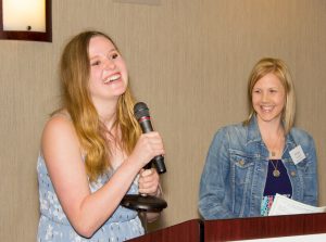Two smiling women. One with microphone at presentation