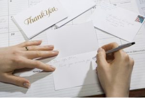 A hand writes thank you notes on a desk.