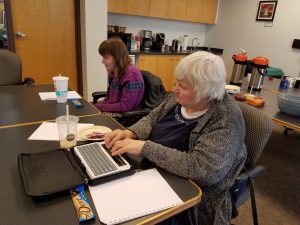 Two women at a table, one using a braille typewriter