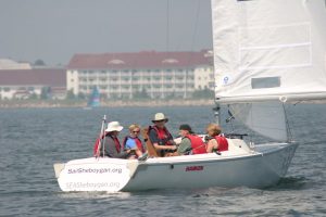A sailboat with five people in it makes its way through a harbor.