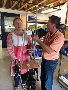 A man and woman hold onto a tall metal and wood object with an audio box on the top.