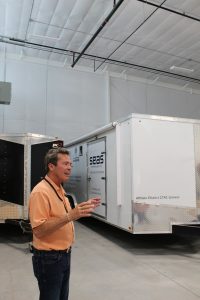 A man talking with his hands standing in front of a trailer.