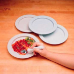 A hand holds a spoon that is scooping up pasta on an inner lip plate.