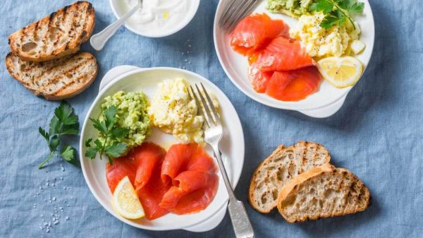 Two plates of eggs, salmon, lemon, bread and guacamole.