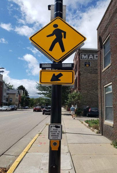 A yellow pedestrian sign and accessible pedestrian signal button.