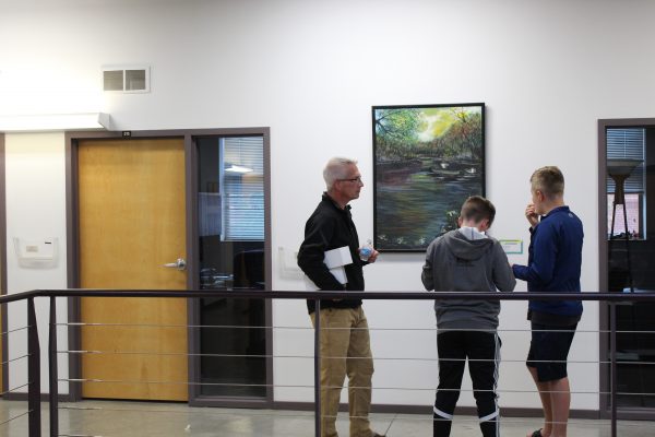 Two boys and a man stand in front of a large oil pastel painting.