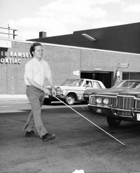 Man with white cane walking across the street