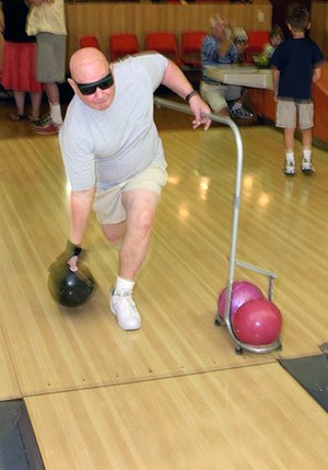A man bowls wearing dark glasses and using a guide rail.