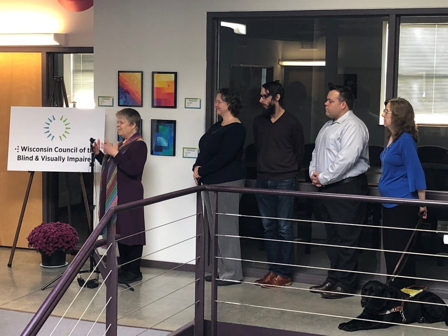 Five people stand next to the Council logo. One person has a service dog and one person has a white cane.