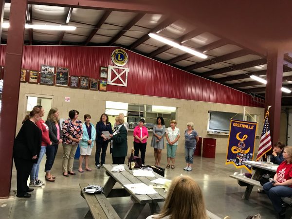 A group of women stand surrounded by Lions Club signs.