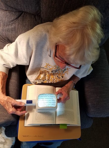 A woman reads a book using a magnifier.