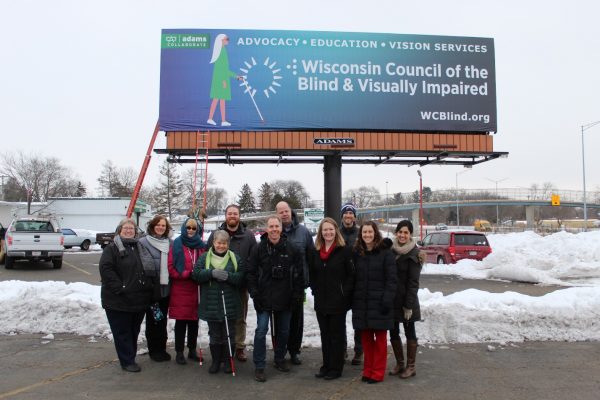 Eleven people stand outside with a billboard behind.