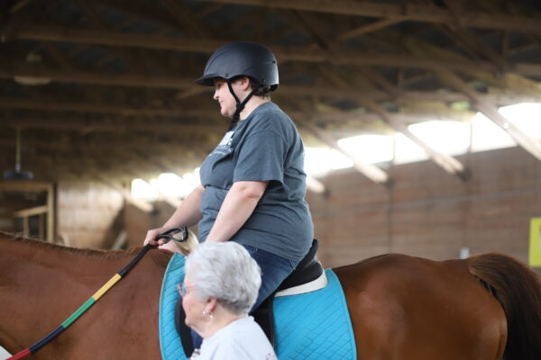  A woman on top of a horse with an instructor next to the horse.