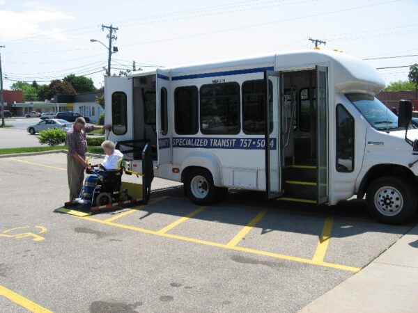 A paratransit rider in a wheelchair is helped out of a van.