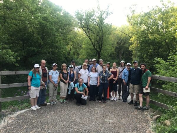 A group of 20 people stands outside on a nature trail.