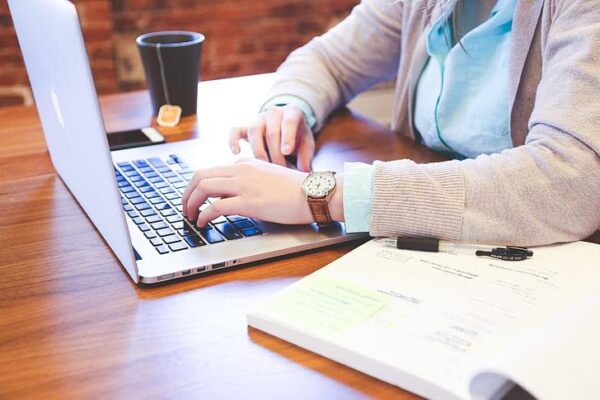 A person with a notebook, laptop and tea.
