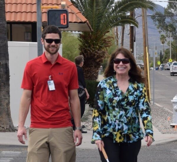 2 people walking down a street together, one is using a cane.