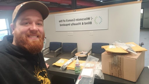 A guy stands in front of packages, Purell and the WCBVI logo.