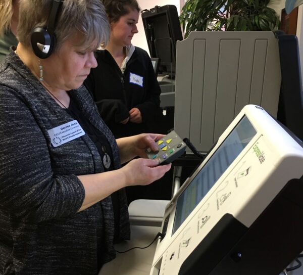 A woman using accessible voting equipment, wearing headphones and holding a tactile marking device