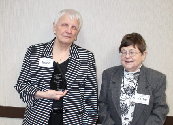 Two woman standing, one holding an award.