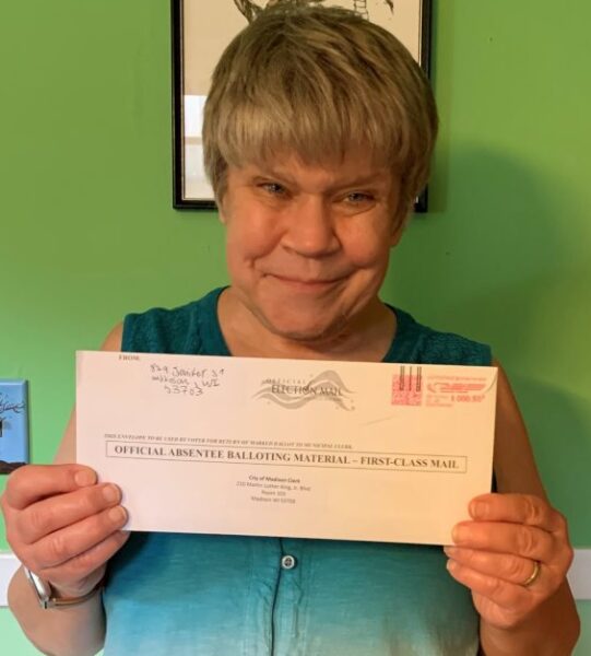 A woman holds up an absentee ballot envelope.