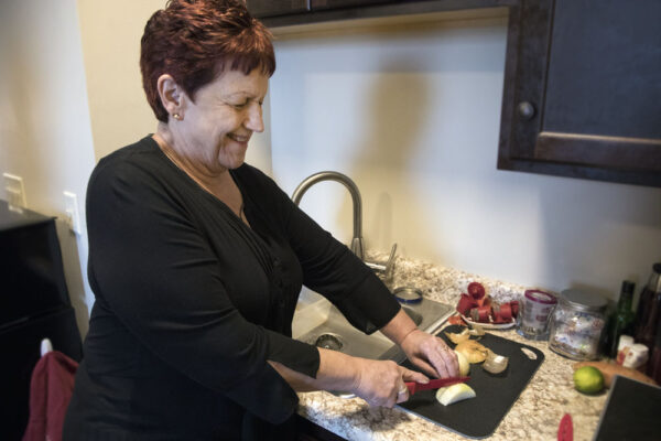Council client Carol uses a high-contrast cutting board and safe slicing technique to slice onions in her apartment.