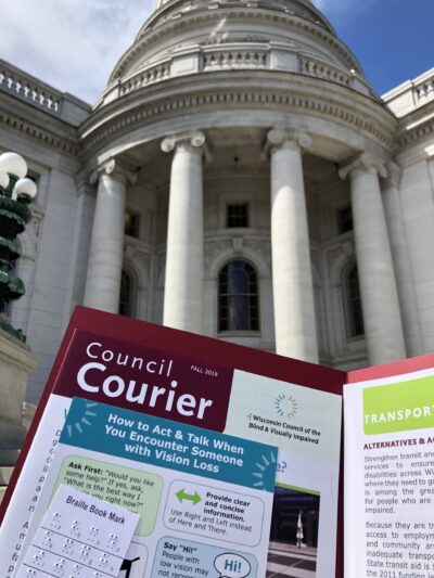 A folder containing a Council Courier, braille bookmark and a handout on transportation in front of the capitol building.