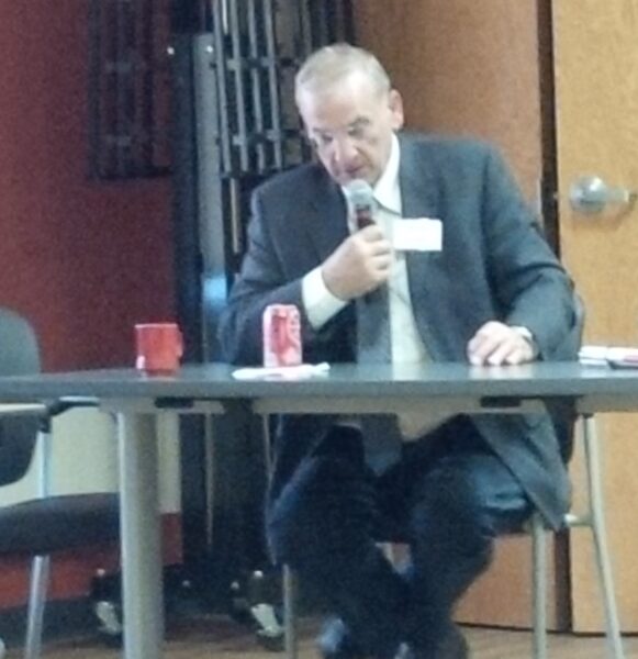 Wearing a business suit, Dan Sippl speaks into a microphone.