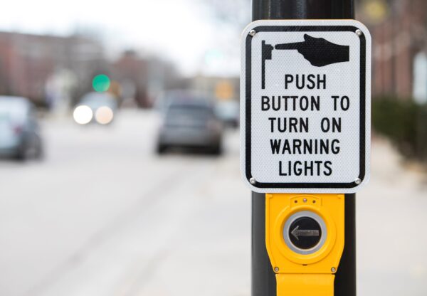 An Accessible Pedestrian Signal with large button and sign directing users to push to turn on warning lights.