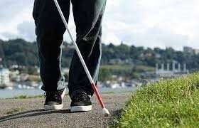 A person walking on a trail, wearing tennis shoes and using a white cane.