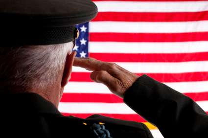 A man, wearing a military uniform, stands with his back to the camera, saluting a United States flag.