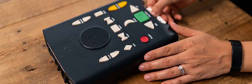 Close-up view of a person’s hands inserting a cartridge into a digital talking book player.