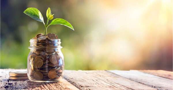 A glass jar full of coins with a plant on a table.