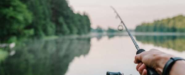 A hand holding a fishing rod extended out over a lake.