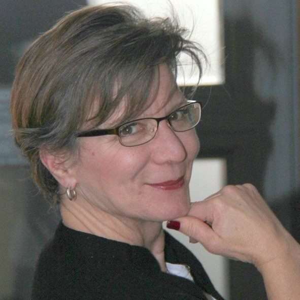 A woman with glasses holding chin smiling at the camera.
