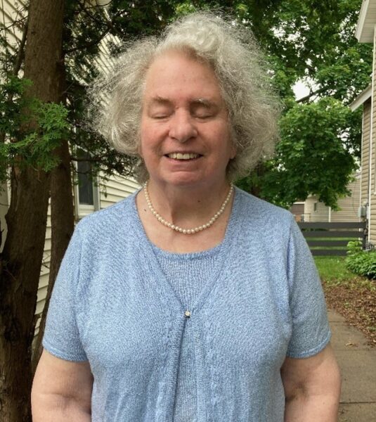 A woman from the waist up with silver hair and a pearl necklace.