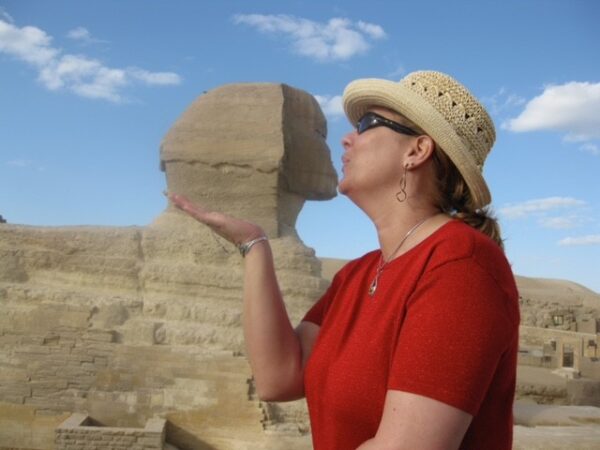 A woman posing by an Egyptian sphynx to create the illusion that she is kissing it.